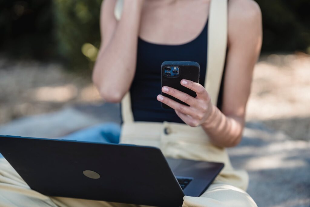 crop businesswoman with laptop using smartphone outside