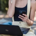 crop businesswoman with laptop using smartphone outside